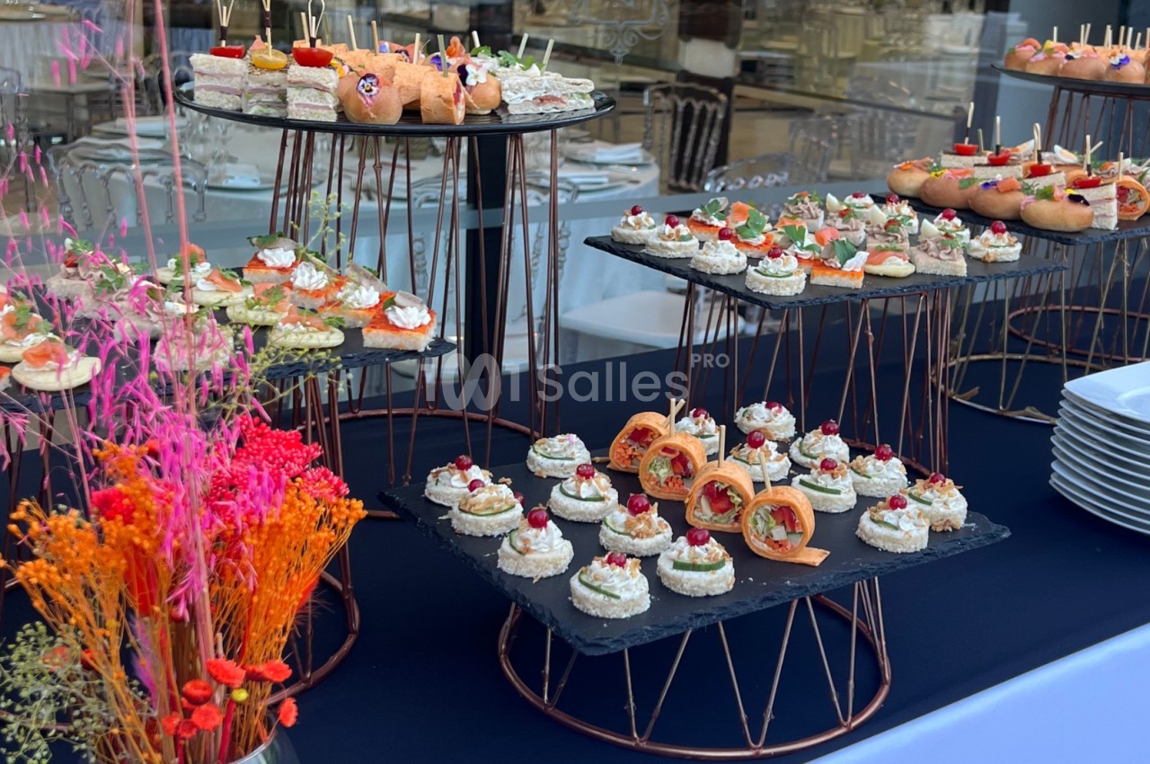 Plateaux de canapés variés disposés sur des présentoirs en métal, avec un bouquet de fleurs colorées au premier plan.