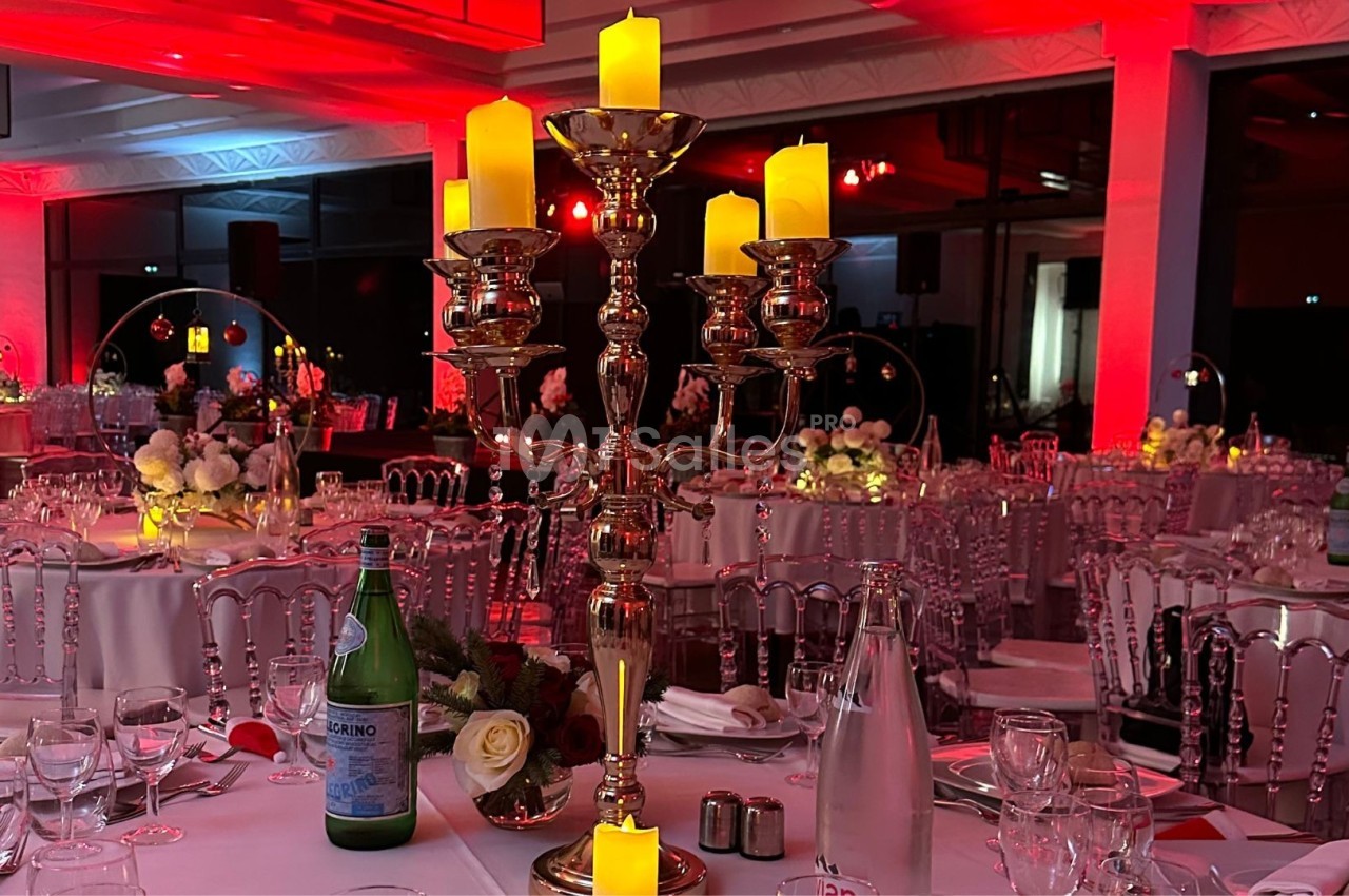 Chandelier doré avec bougies allumées sur une table élégamment dressée dans une salle éclairée de rouge.