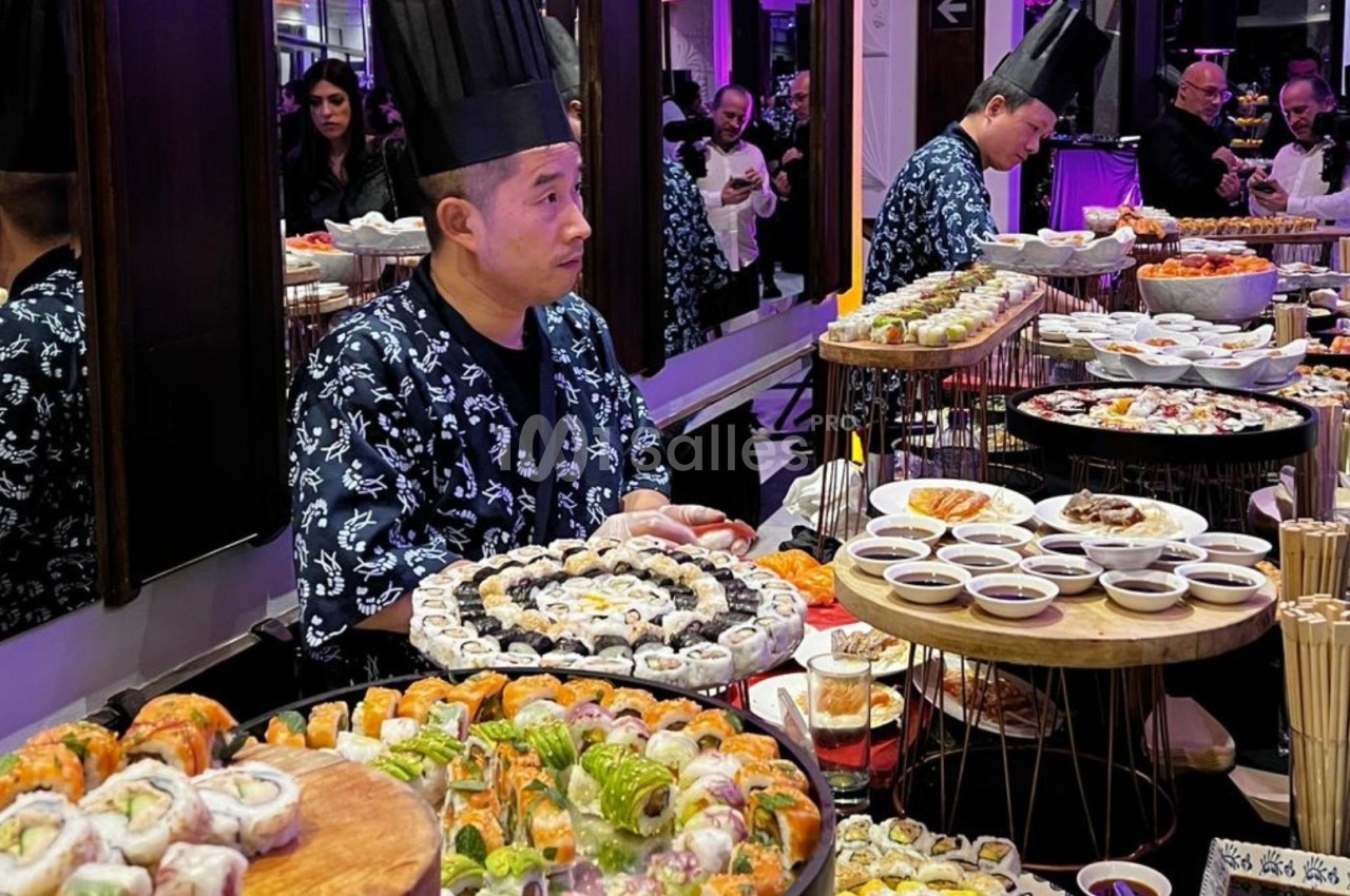 Un chef prépare et présente un buffet varié de sushis et plats japonais dans un cadre élégant.