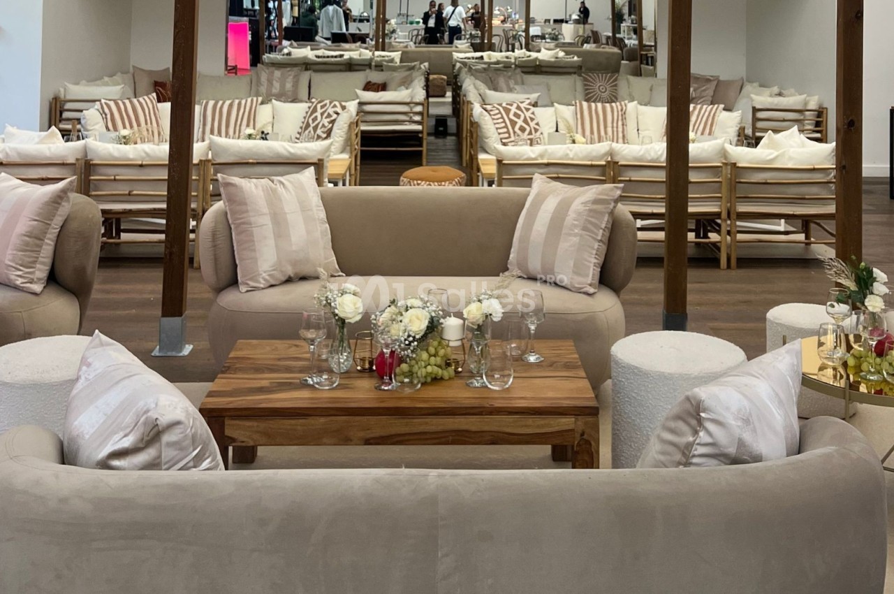 Salon élégant avec canapés beiges, table basse en bois décorée de fleurs et verres, dans un espace lumineux et moderne.