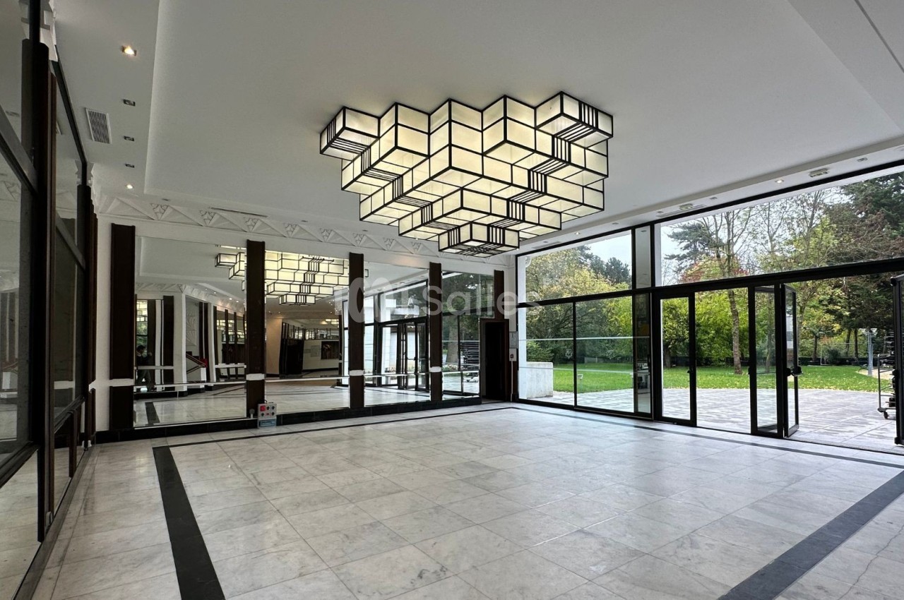 Hall spacieux avec sol en marbre, grandes baies vitrées donnant sur un jardin et un lustre géométrique suspendu.