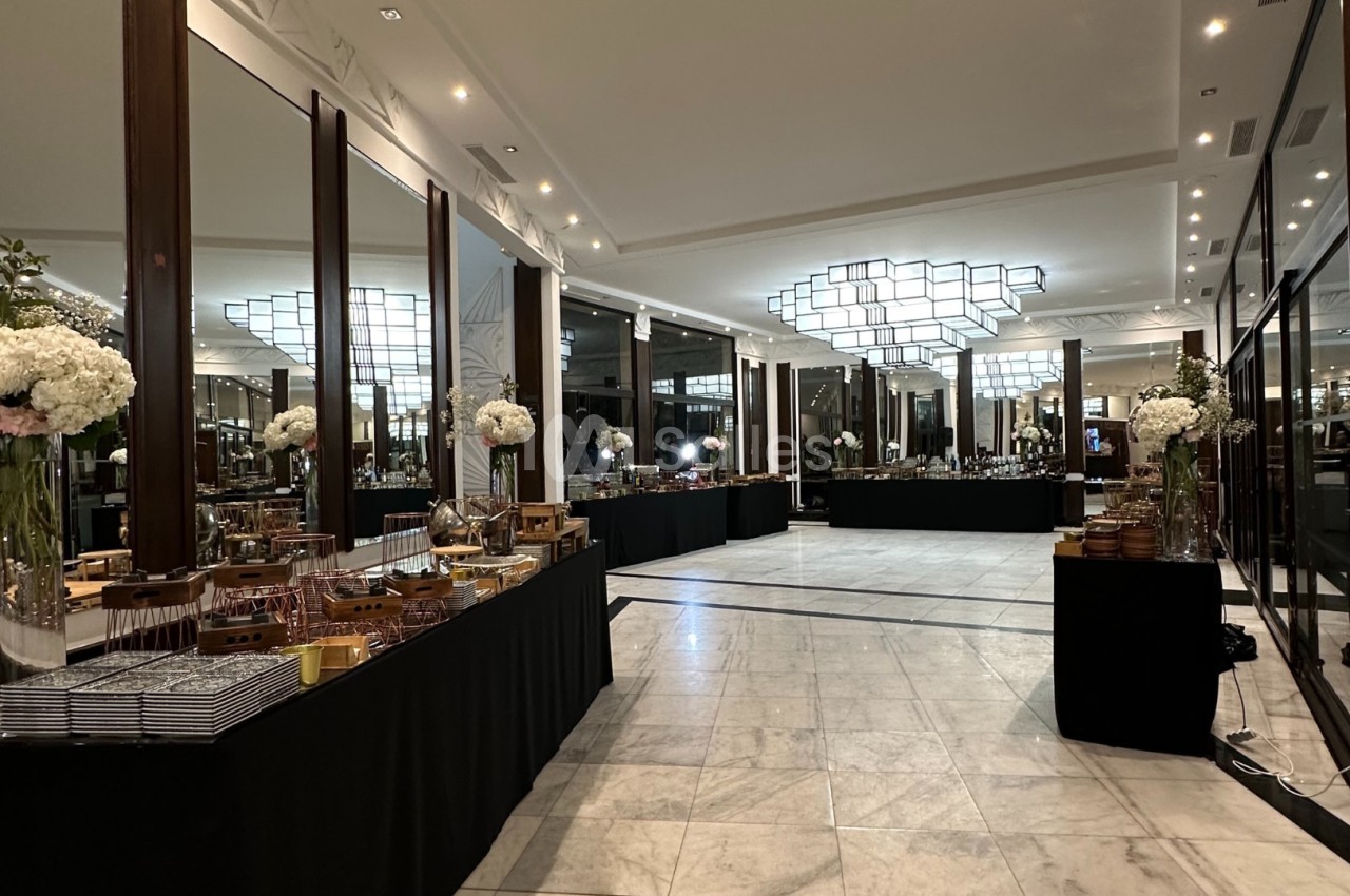Salle élégante avec tables de buffet alignées, décorée de fleurs blanches et éclairée par un grand lustre moderne.