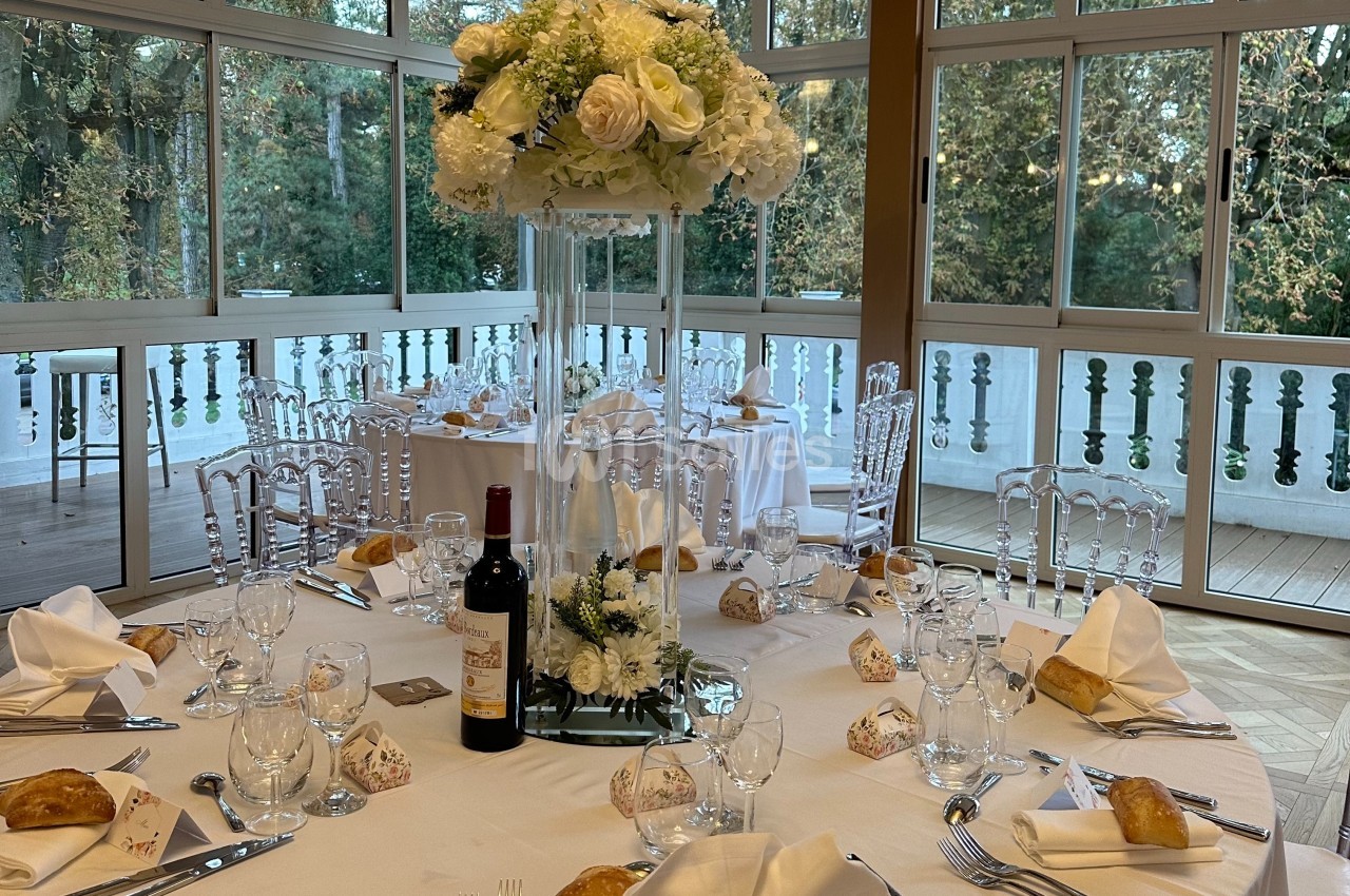 Table de réception élégamment dressée avec un centre de table floral, entourée de chaises transparentes, dans une salle…