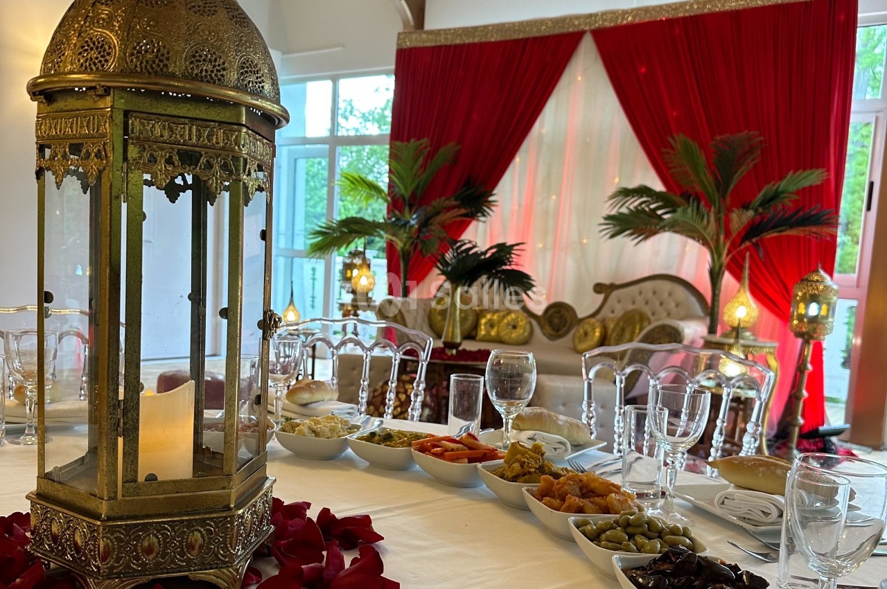 Table décorée avec une lanterne dorée, des plats variés et un décor oriental en arrière-plan avec rideaux rouges.