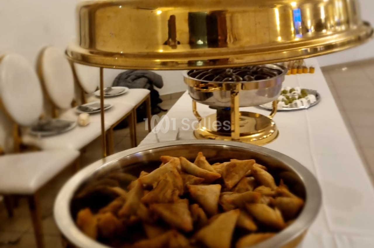 Assortiment de samoussas dans un plat en métal, avec d'autres mets disposés sur une table de buffet.