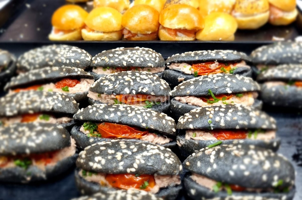 Sandwichs au pain noir garnis de thon, tomates confites et herbes, disposés sur un plateau devant des mini-burgers.