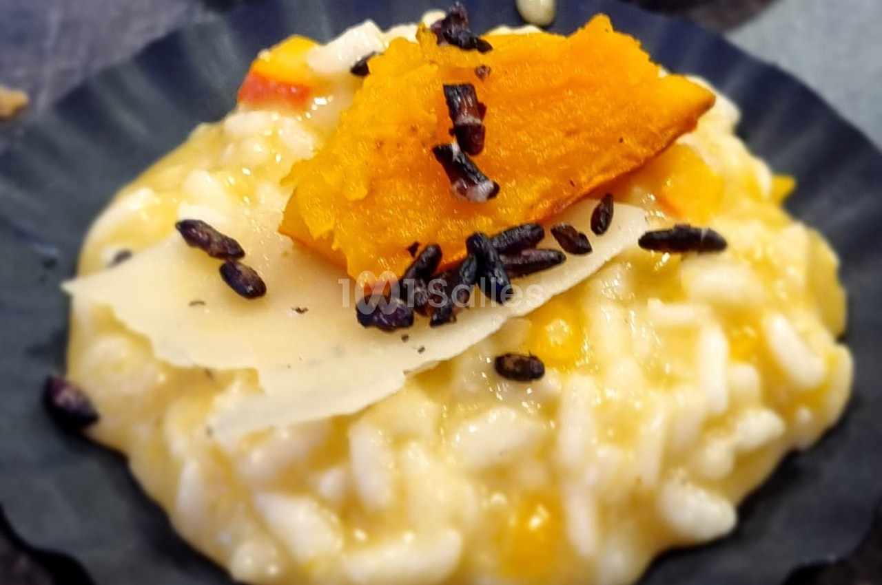 Risotto crémeux garni de copeaux de parmesan, morceaux de courge rôtie et riz noir croustillant.