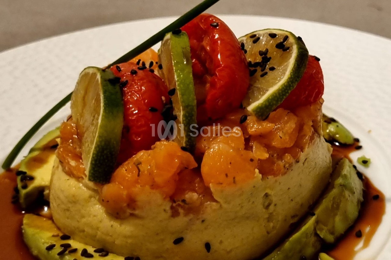 Assiette garnie d'une mousse verte, saumon mariné, tomates cerises, rondelles de citron vert et graines noires.
