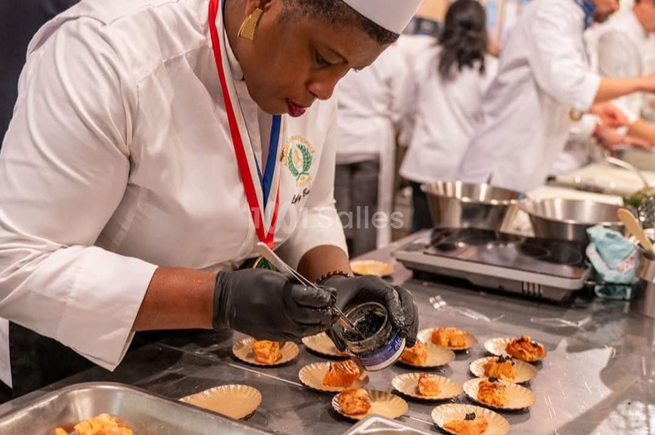 Une cheffe en tenue professionnelle dispose soigneusement un ingrédient sur des assiettes individuelles en cuisine.