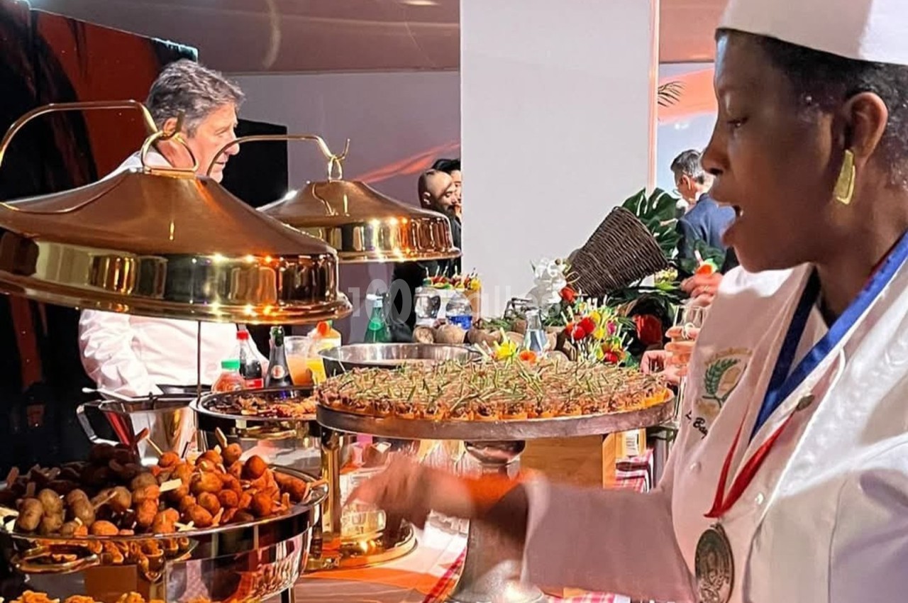 Un chef et une cuisinière en tenue professionnelle préparent et présentent des plats sur un buffet garni.