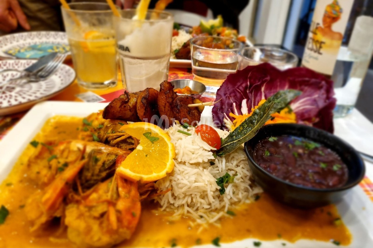 Assiette de crevettes en sauce avec riz, légumes, crudités et accompagnements, servie sur une table dressée.