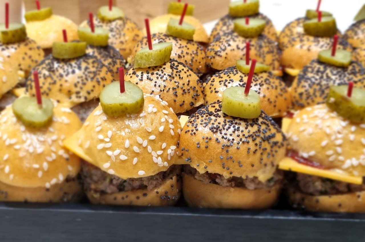 Plateau de mini-burgers garnis de fromage, cornichons et piques rouges, avec pains aux graines de sésame et pavot.