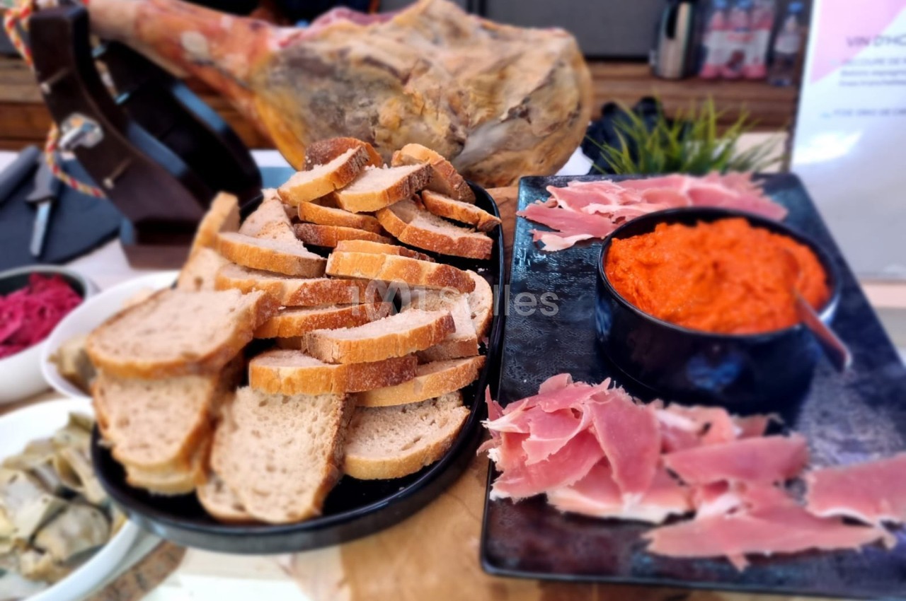 Plateau avec tranches de pain, jambon cru, bol de sauce rouge et arrière-plan flou avec un jambon entier.