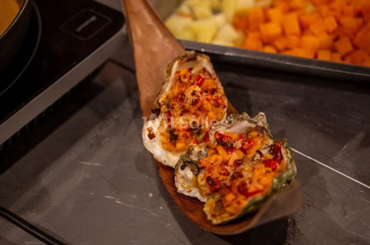 Huîtres gratinées garnies de fromage et épices, présentées sur un plateau en bois, avec légumes en arrière-plan.