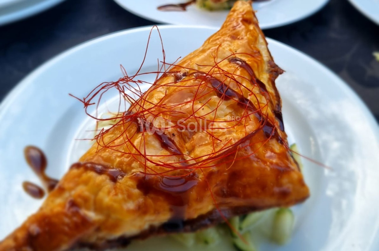 Feuilleté doré garni, nappé de sauce et décoré de filaments rouges, servi sur une assiette blanche.