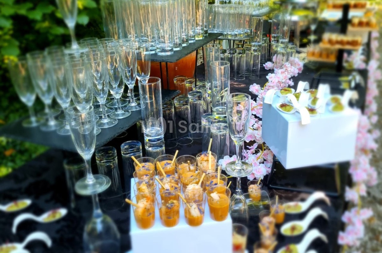 Buffet avec verrines colorées, flûtes en verre et décor floral disposés sur des tables en extérieur.