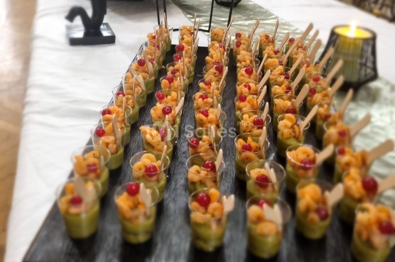 Verrines alignées sur un plateau, contenant des crevettes, de l'avocat et des tomates cerises, avec des cuillères en bois.