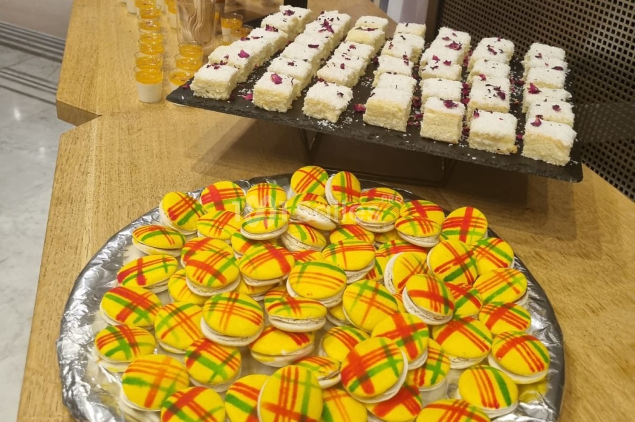 Plateau de macarons colorés et assiette de petits gâteaux décorés de pétales, présentés sur une table en bois.