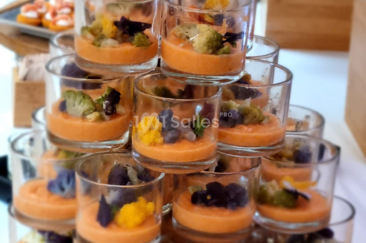 Verrines empilées contenant une mousse orange garnie de fleurs comestibles et de légumes colorés.