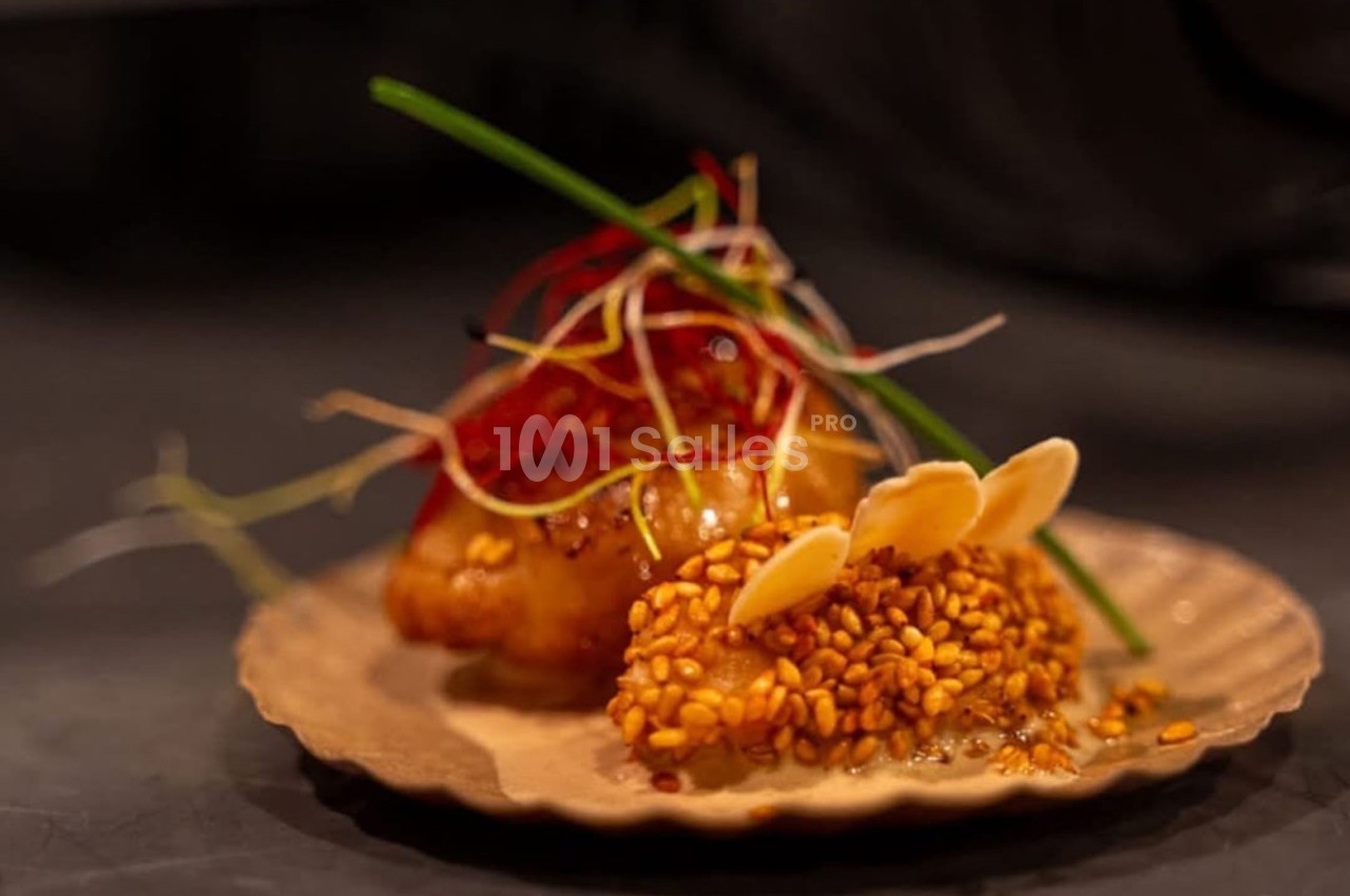 Assiette garnie d'une préparation culinaire sophistiquée avec graines de sésame, amandes effilées et décorations végétales.