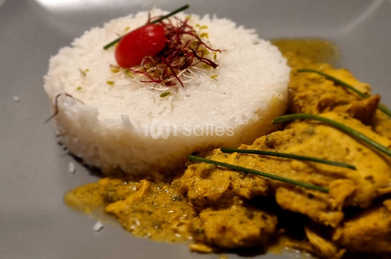 Assiette avec du riz blanc moulé, garni d'une tomate cerise et d'herbes, accompagné de poulet en sauce jaune.