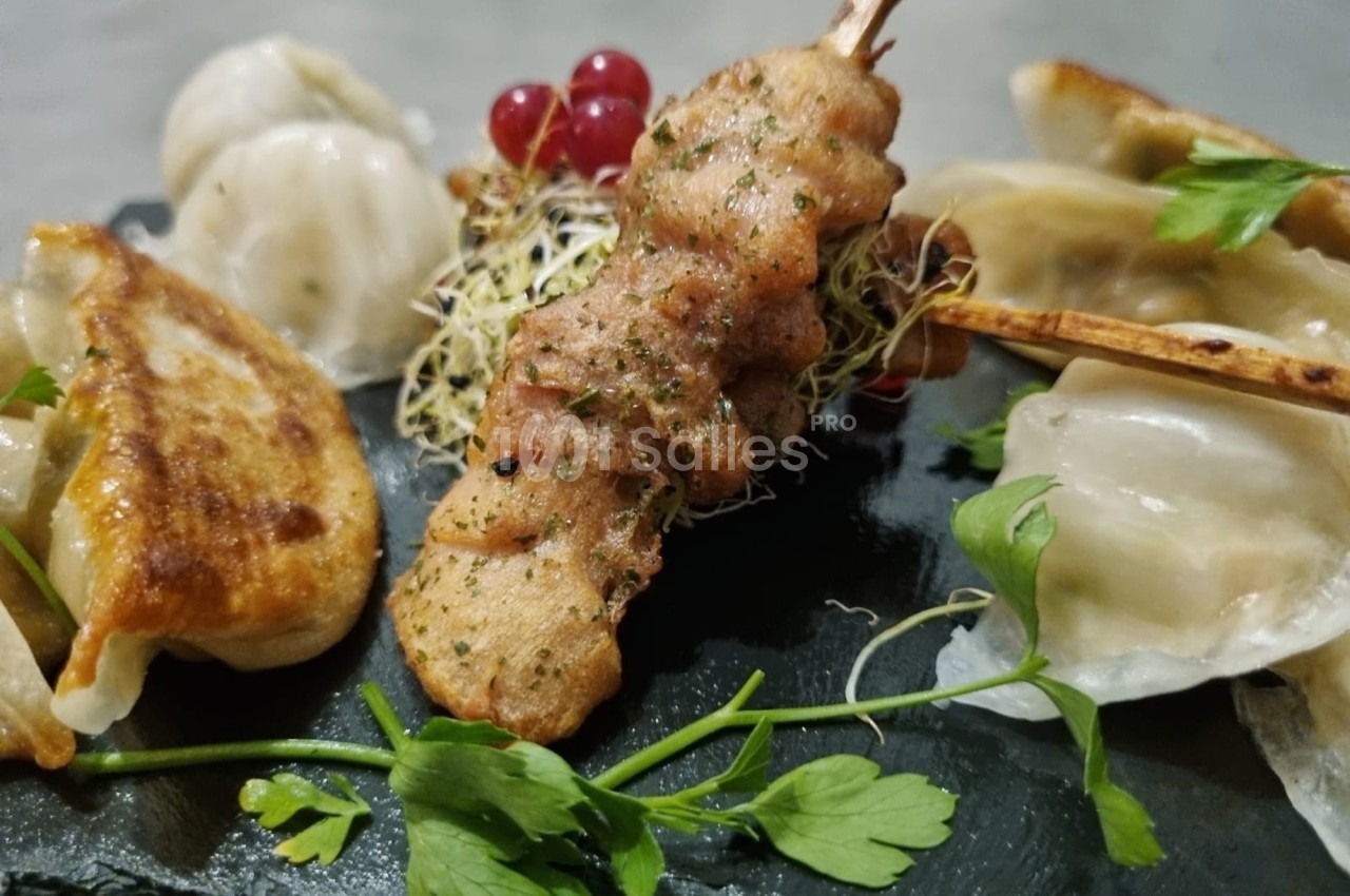 Assortiment de raviolis grillés et vapeur avec une brochette de viande, décoré de pousses et de groseilles rouges.