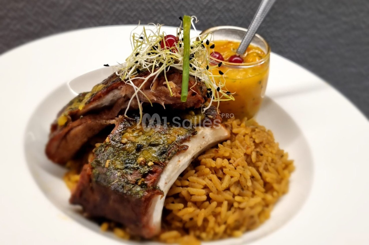 Plat de côtes de porc grillées avec herbes, servi sur du riz épicé, accompagné d'une sauce mangue et groseilles.