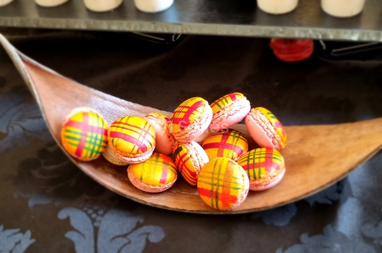 Macarons colorés avec motifs à carreaux rouges et jaunes, présentés sur une cuillère en bois décorative.
