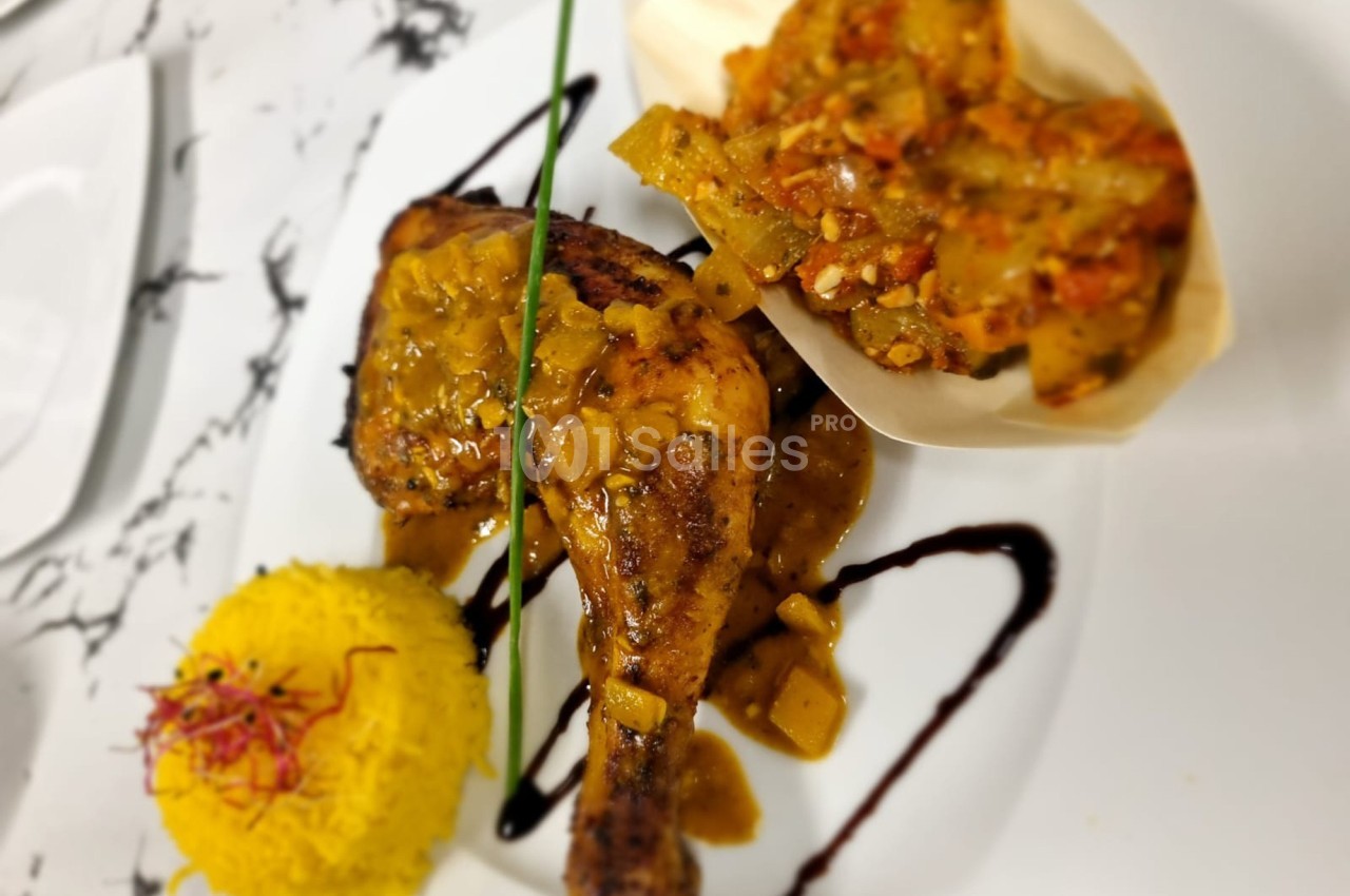 Poulet rôti avec sauce épicée, accompagné de riz safrané et légumes mijotés, présenté sur une assiette blanche.