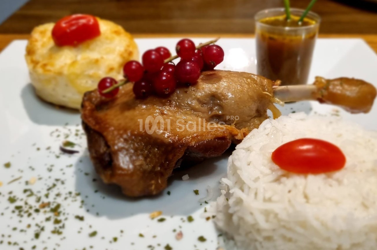 Assiette composée d'une cuisse de canard, riz, gratin, groseilles et sauce servie dans un verre.