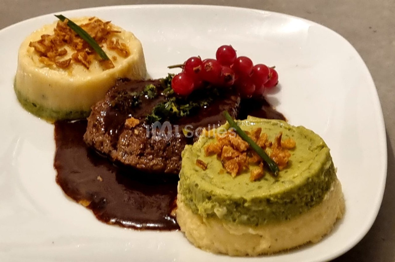 Assiette avec un steak nappé de sauce, accompagné de purées de légumes et décoré de groseilles rouges.