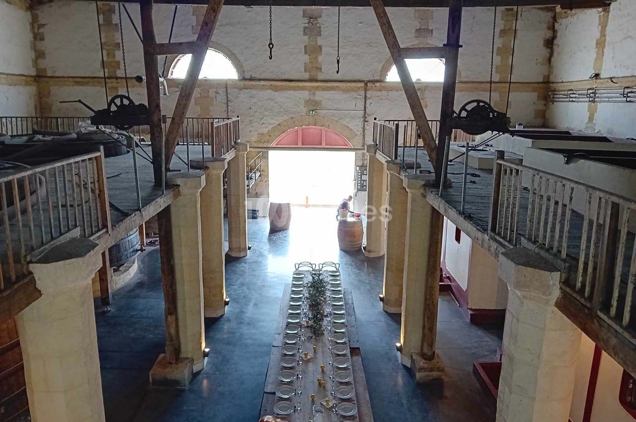 Intérieur d'un bâtiment en pierre avec une grande table dressée au centre, entourée de balcons en bois.
