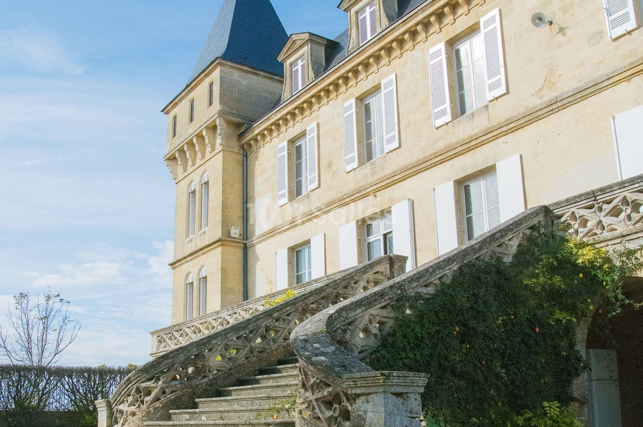 Façade d'un château en pierre avec escalier en pierre orné de balustrades, sous un ciel bleu dégagé.
