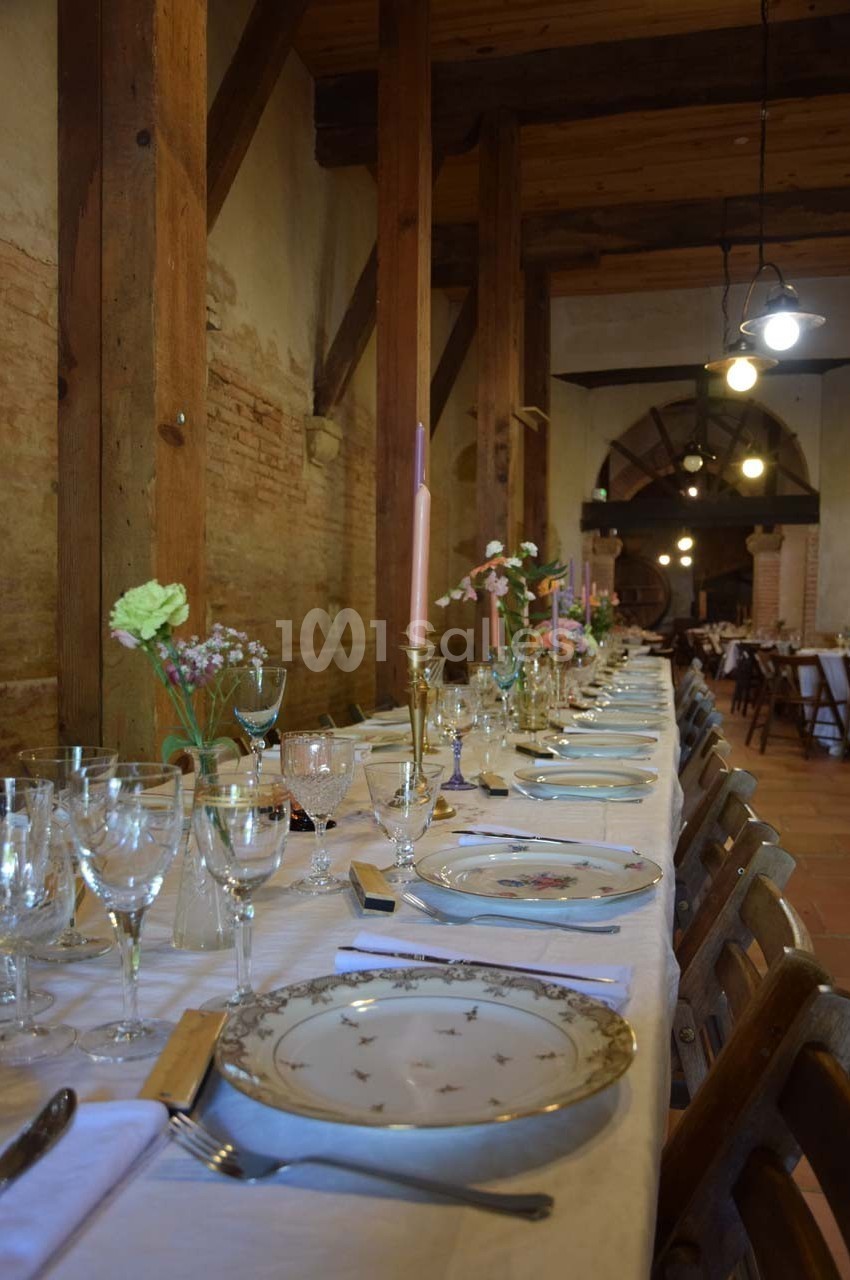 Table dressée avec vaisselle élégante, bougies et fleurs, dans une salle rustique aux murs en briques et poutres apparentes.