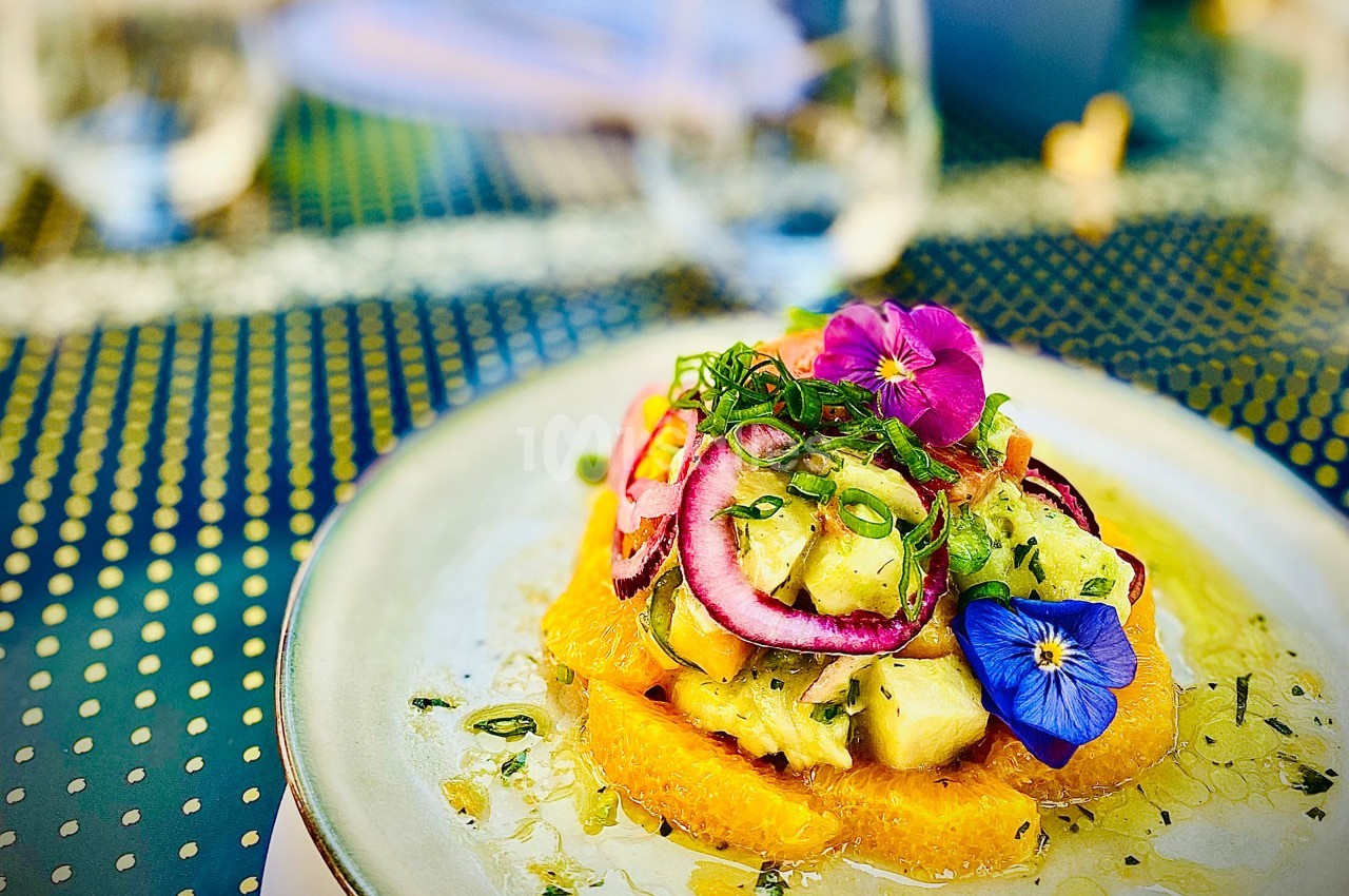 Assiette de salade colorée avec fruits exotiques, fleurs comestibles et herbes fraîches sur une table extérieure.