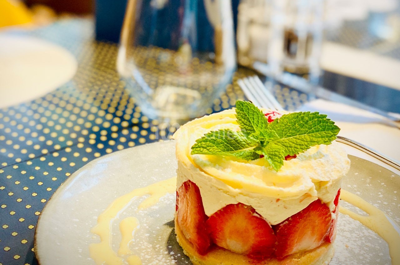 Dessert composé de fraises fraîches, crème chantilly et biscuit, décoré d'une feuille de menthe, servi sur une assiette.