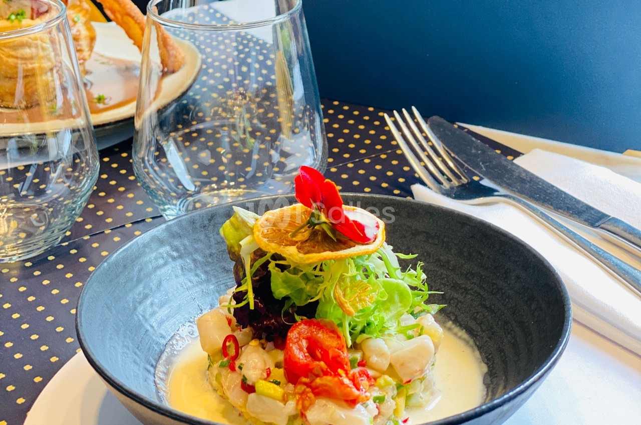 Plat de ceviche servi dans un bol noir, garni de salade, rondelle de citron séché et fleurs comestibles.