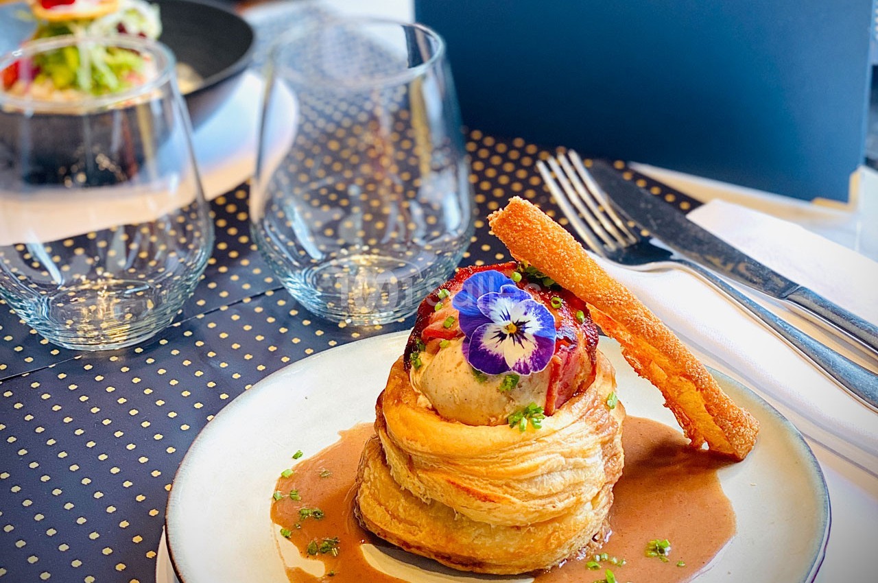 Plat gastronomique composé d'une pâte feuilletée garnie, décorée de fleurs comestibles et accompagnée d'une sauce.