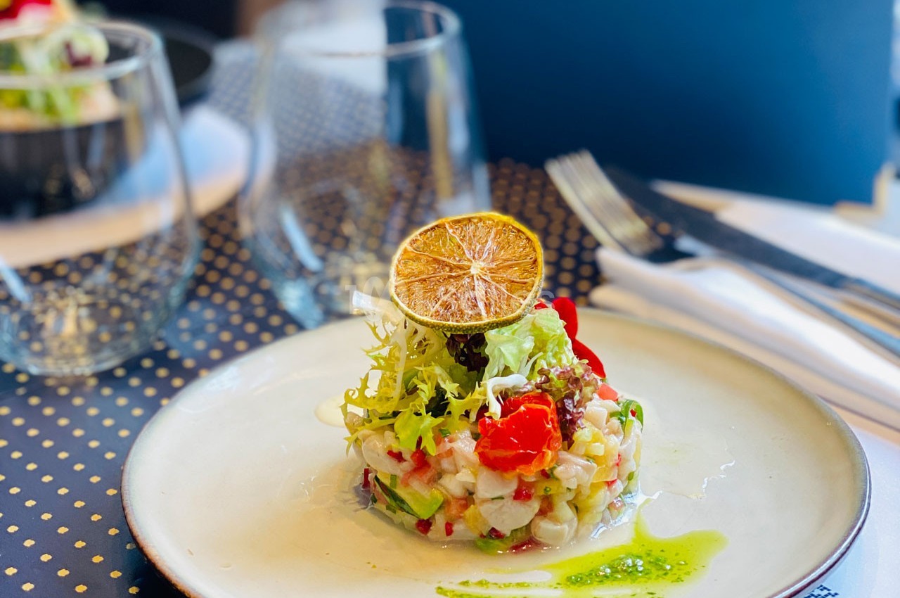 Assiette de ceviche dressée avec des légumes, herbes fraîches et une rondelle de citron séché, servie sur une table élégante.