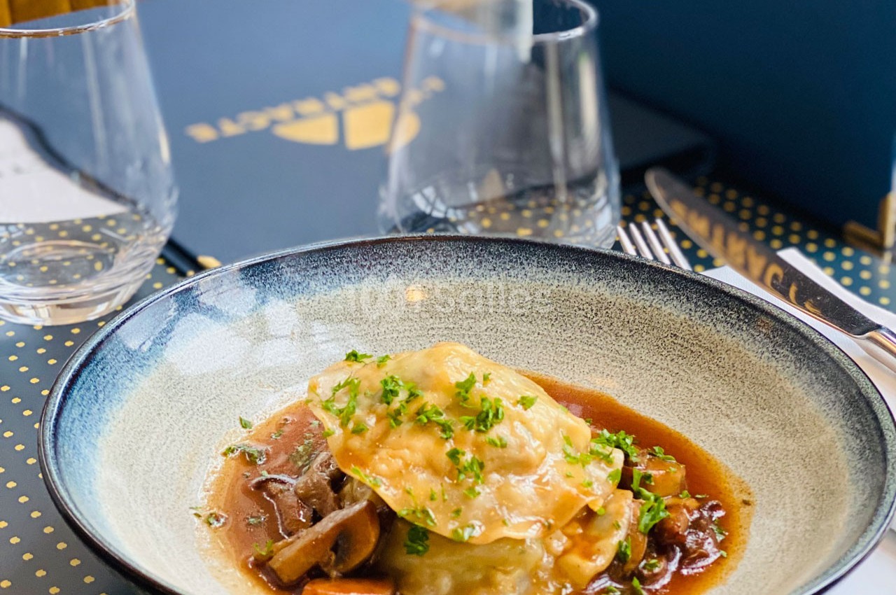 Assiette de ravioles garnies, servies avec une sauce brune et des champignons, décorée de persil haché.