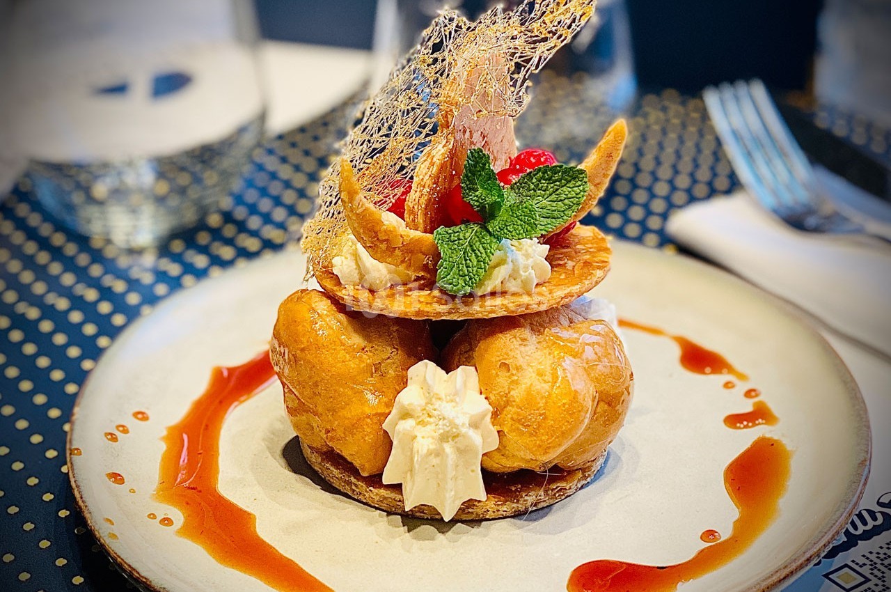 Dessert raffiné composé de choux, crème, caramel et décorations gourmandes sur une assiette blanche.