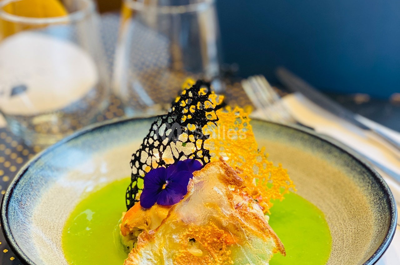 Plat gastronomique avec une présentation soignée, comprenant une sauce verte, des décorations croustillantes et une fleur…