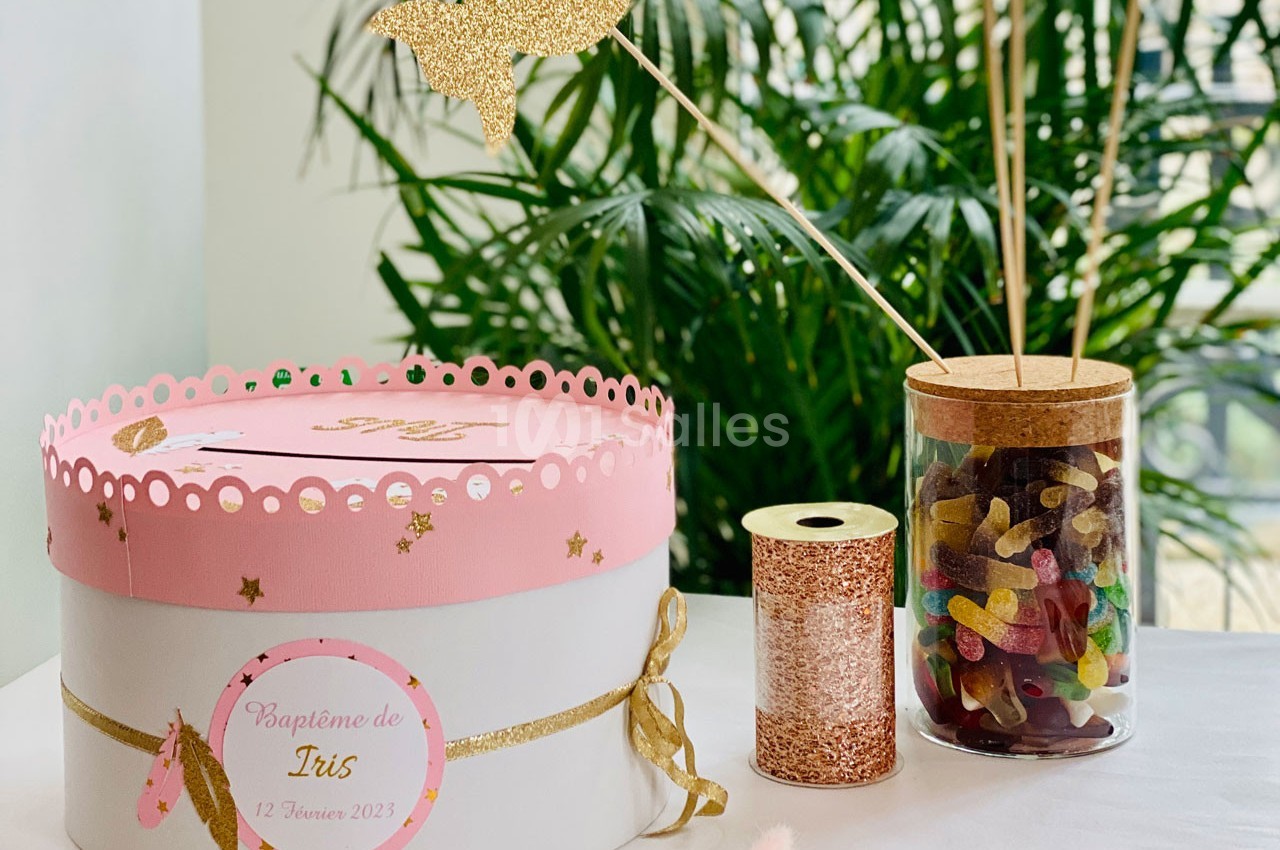 Boîte décorative rose et blanche pour un baptême, accompagnée d'un pot de bonbons et d'éléments dorés sur une table.