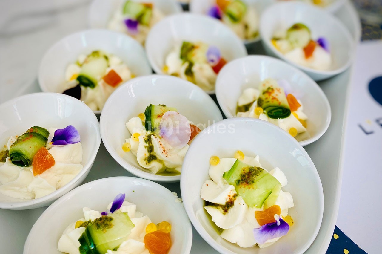 Assortiment de verrines avec fromage frais, tranches de concombre, fleurs comestibles et garnitures colorées.