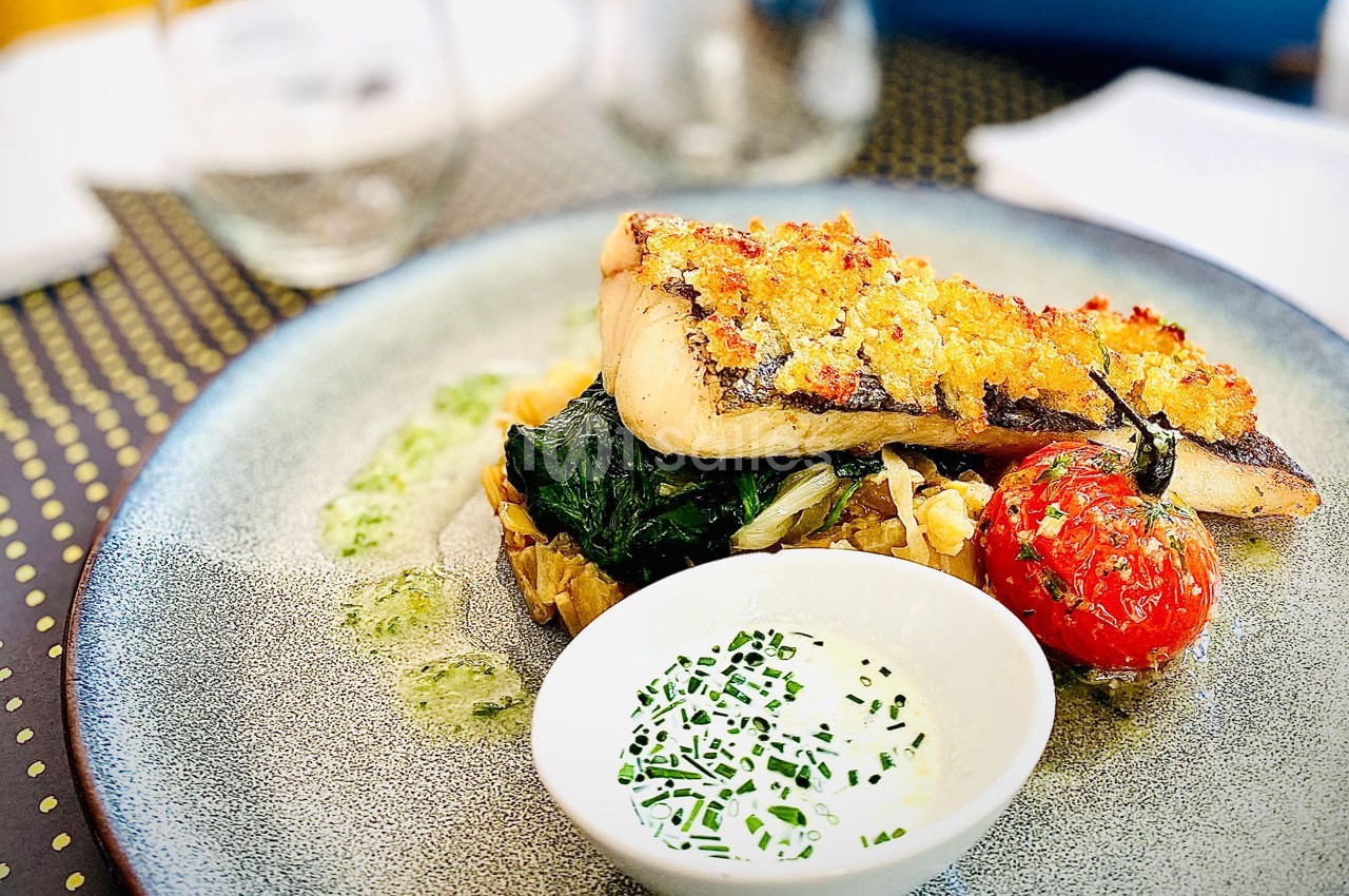 Plat de poisson grillé avec croûte dorée, légumes sautés, tomate rôtie et sauce blanche garnie de ciboulette.