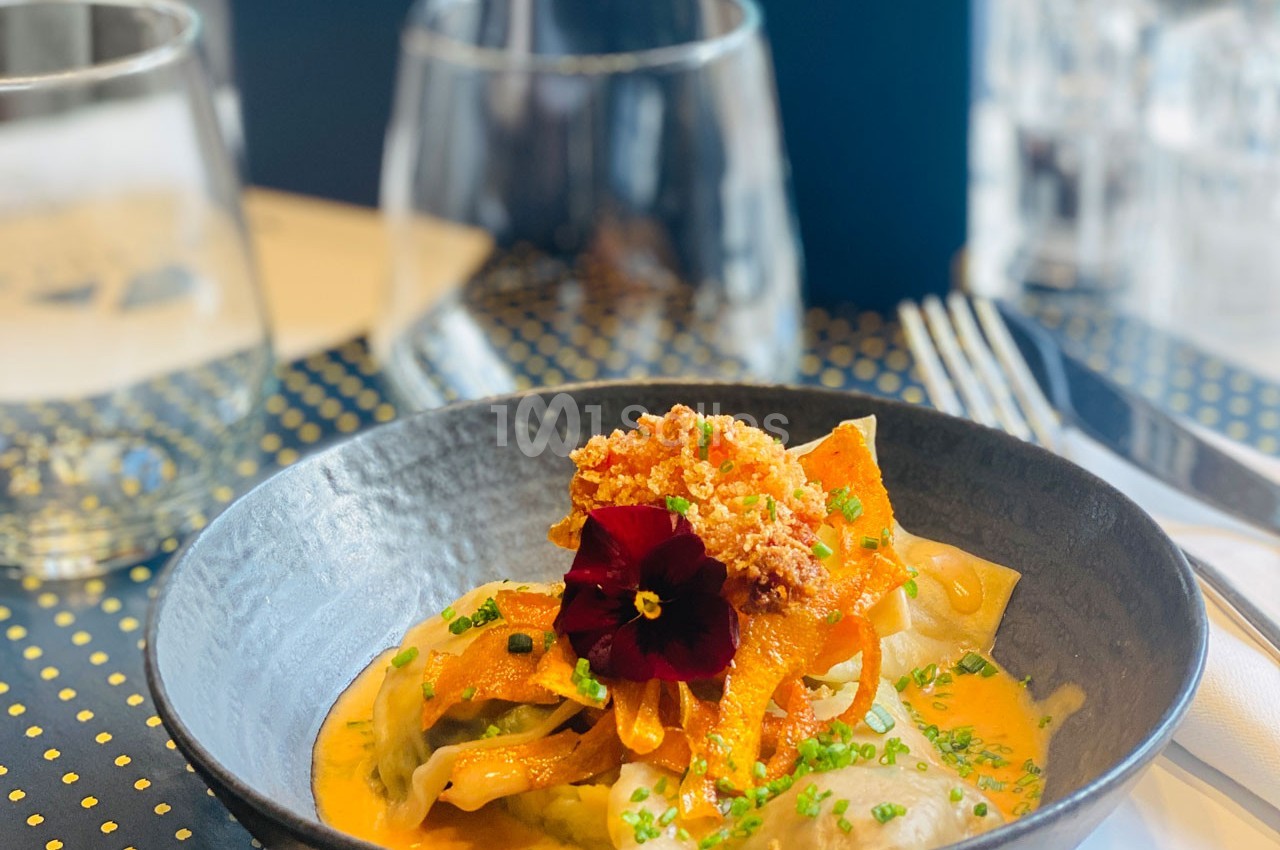 Assiette de ravioles garnies de légumes, sauce crémeuse orange, décorée d'une fleur comestible et de ciboulette.