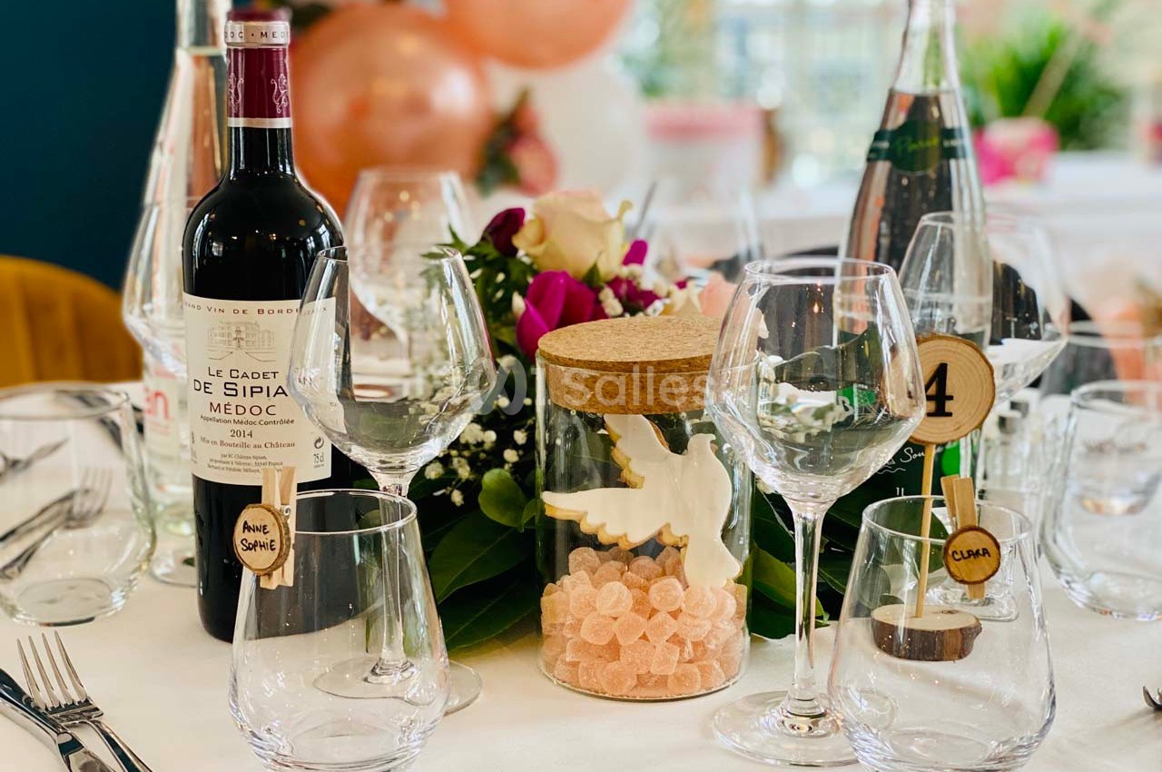 Table décorée avec des verres, une bouteille de vin, des fleurs, des bonbons et des ballons en arrière-plan.