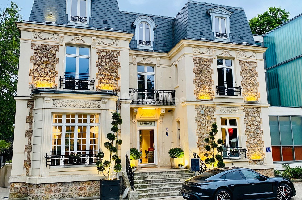 Façade d'une maison bourgeoise en pierre et briques, avec un escalier central et une voiture noire garée devant.