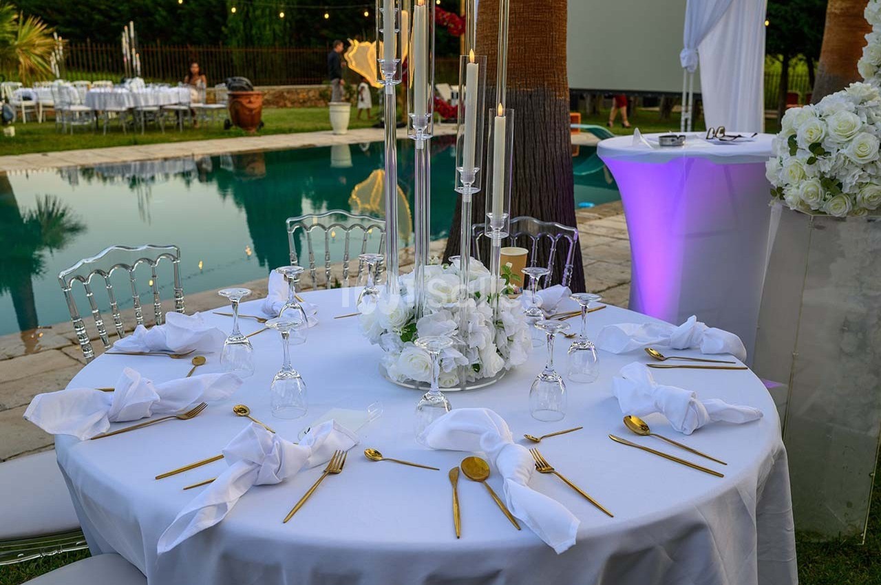 Table élégamment dressée avec des couverts dorés, serviettes blanches et centre de table floral, près d'une piscine.