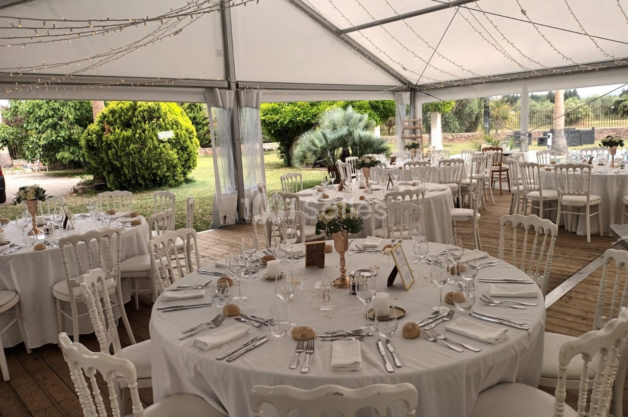 Salle de réception sous une tente avec tables rondes dressées, nappes blanches et décoration élégante.
